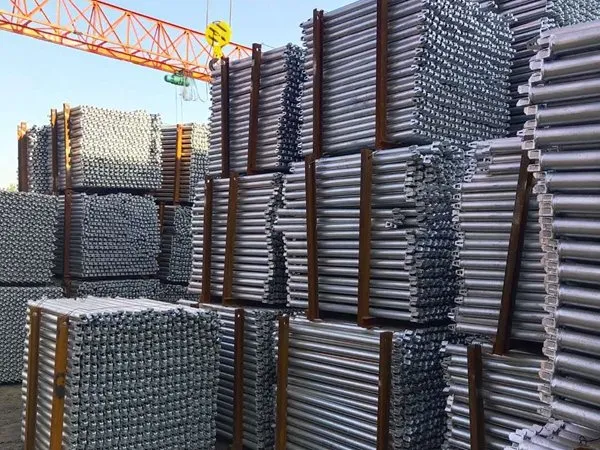 Bundled galvanized standards stacked under a gantry crane